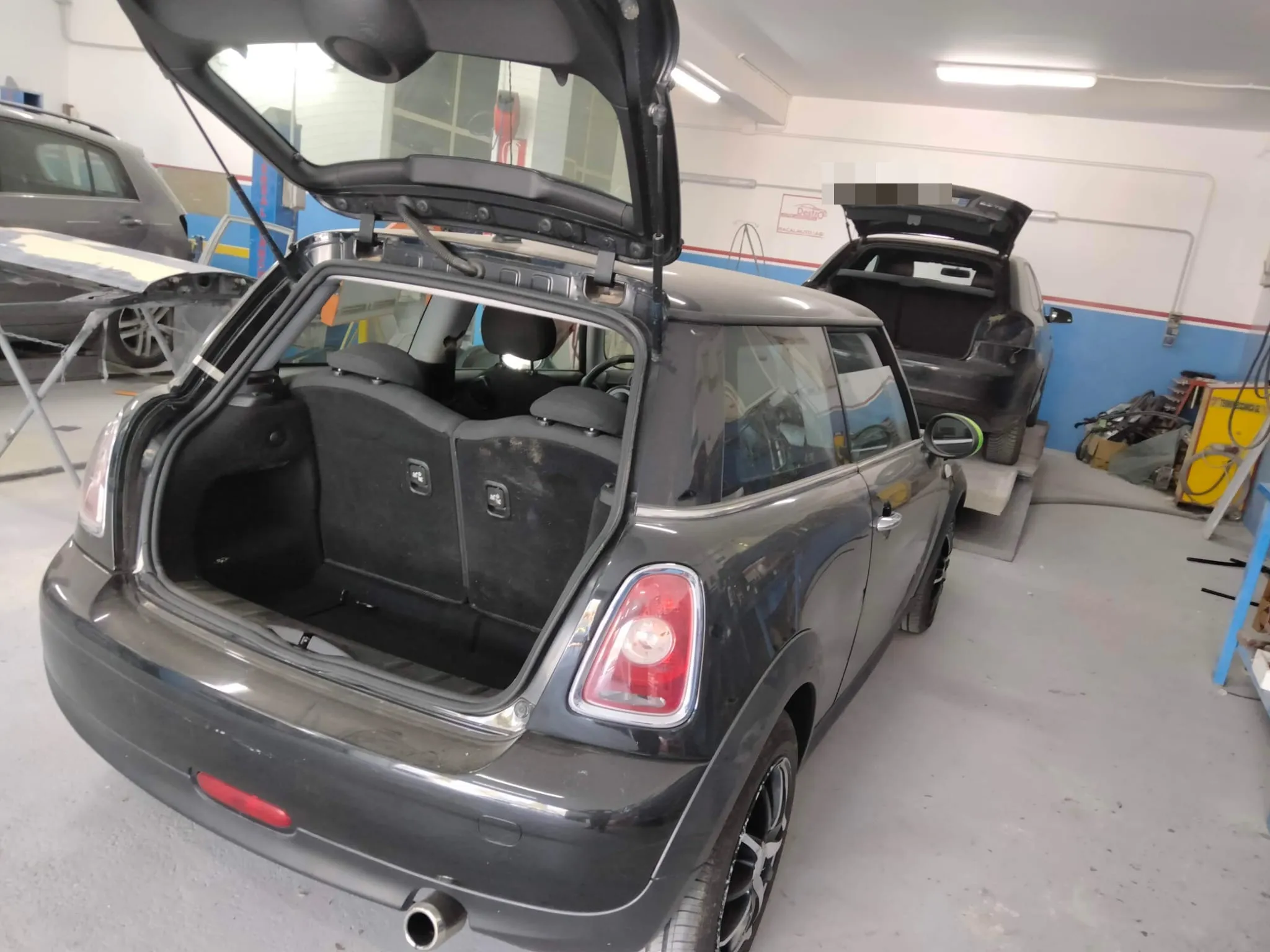 Mini Cooper nera danneggiata, portellone posteriore aperto in officina